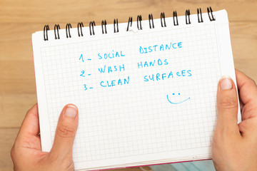 Coronavirus COVID-19 health safety guidelines. hands holding notebook with rules, practice social distancing, wash hands, clean surfaces, hand washing, stay home.
