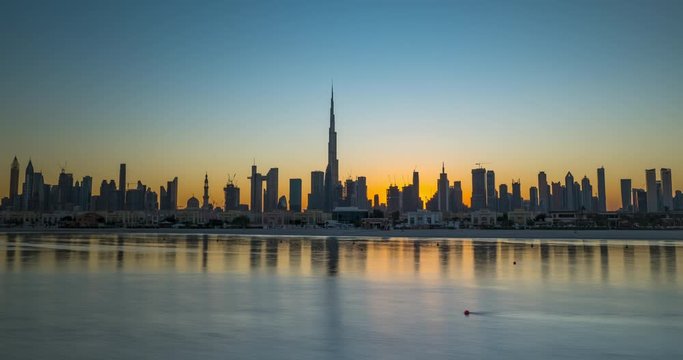 Sunrise in Dubai hyperlapse or timelapse view from boat or sea. The Sun rises over UAE skyscrapers at morning. Camera moves along beach, coast, shore.