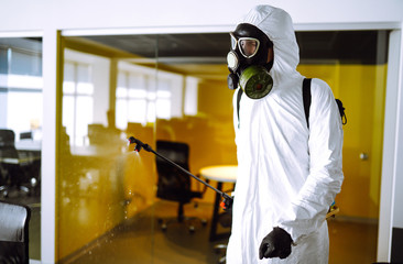 Disinfecting of office to prevent COVID-19, Man in protective hazmat suit with  with spray...
