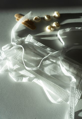 Close-up of white medical remedies. Non-woven mask with ties, fingertips, plasters. Light neutral background, bright lighting, contrasting shadows.
