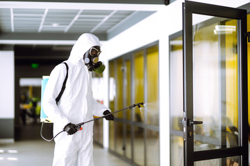 Disinfecting of office to prevent COVID-19, Man in protective hazmat suit with  with spray...