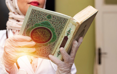 muslim doctor woman wearing hijab and With Stethoscope holding holy book with Arabic calligraphy...