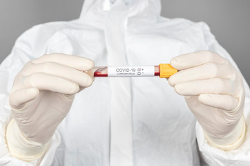 Close-up photo of female doctor holding a blood sample in protective clothes during coronavirus pandemic. Epidemic, pandemic of coronavirus covid 19. Doctor, patient in respirator