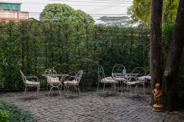 Outdoor view with shady atmosphere of cafe with vintage white tables and chairs surrounded with green garden on riverside in Thailand.