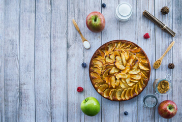 Homemade apple pie surrounded by ingredients on a white wooden surface. Top view and copy-space.