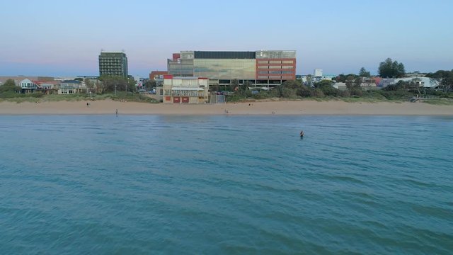Forward flight low over water rising high up revealing Frankston suburb  and South East Water building at sunset in Australia