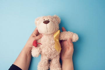female hands hold a small teddy bear with a yellow ribbon folded in a loop