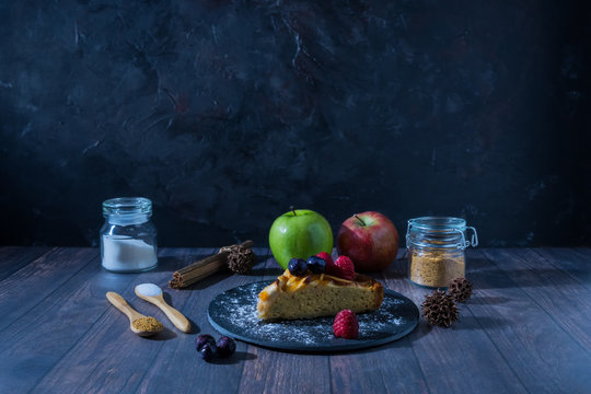 Portion of apple pie surrounded by ingredients on a wooden surface and dark background, Gastronomic concept. - Powered by Adobe