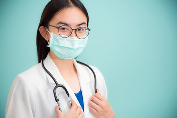 Studio portrait beautiful Asian young woman doctor with stethoscope in white uniform wear glasses and green mask to protect Corona Virus for health looking at camera on green copy space background