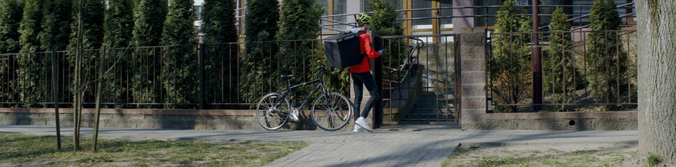 Delivery man courier wearing medical mask ringing at the door of residential building, food delivery to customers during virus outbreak. Coronavirus, COVID-19, safe delivery