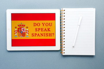 flat lay on a light blue background on the topic of online education, learning Spanish on the Internet: a notebook, pen and tablet with the inscription Do you speak Spanish 