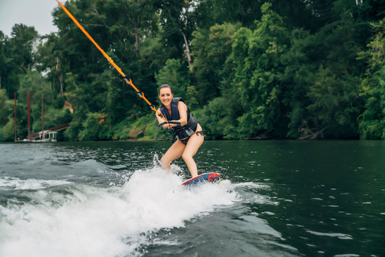 Happy smiling woman wake boarding behind boat on lake surrounded by trees