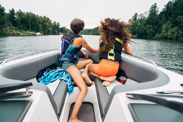 Girls in life jackets sitting on bow of boat on lake surrounded by trees