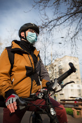 Young man on a bicycle in a medical mask in a city park.