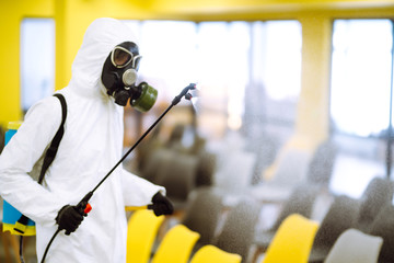 Man wearing protective suit disinfecting assembly hall with spray chemicals to preventing the spread of coronavirus, pandemic in quarantine city. Disinfecting of office. COVID-19.