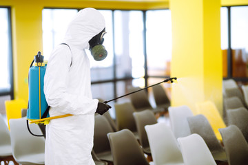 Fototapeta na wymiar Man wearing protective suit disinfecting assembly hall with spray chemicals to preventing the spread of coronavirus, pandemic in quarantine city. Disinfecting of office. COVID-19.