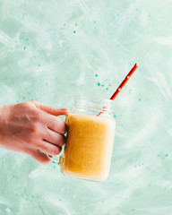 Ripe mango smoothie in a jar on a green background