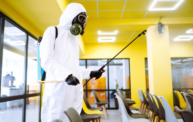 Man wearing protective suit disinfecting assembly hall with spray chemicals to preventing the spread of coronavirus, pandemic in quarantine city. Disinfecting of office. COVID-19.