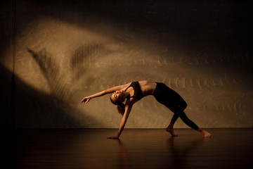 Young Asian woman practicing yoga in moody studio during golden hour
