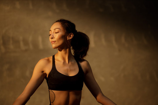 Young Asian woman practicing yoga in moody studio during golden hour