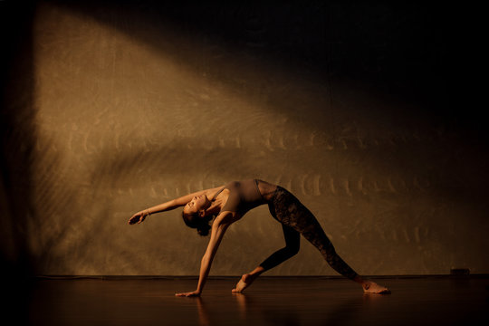 Young Asian woman practicing yoga in moody studio during golden hour