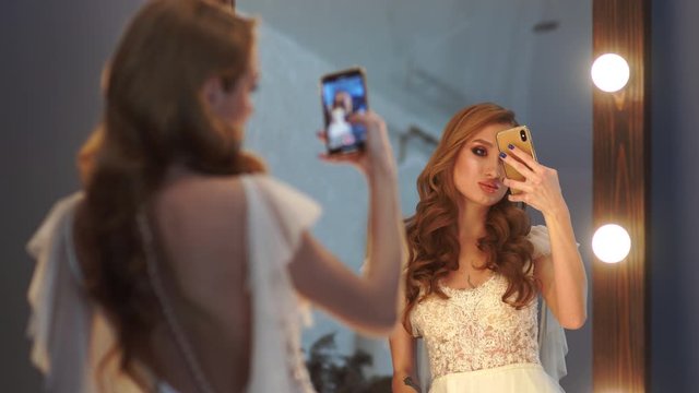 Beautiful girl model posing in front of a mirror and taking pictures on a smartphone.