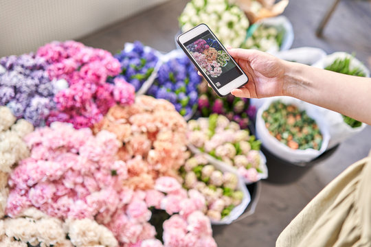 Flowers delivery. A woman florist takes a photo on her phone of flowers. Floral shop concept . Florist woman creates flower arrangement in a wicker basket.