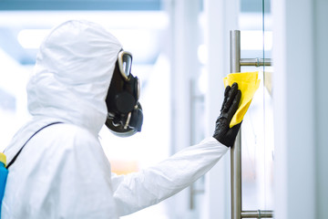 Man in protective hazmat suit washes door handles in office to preventing the spread of...