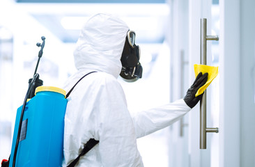 Man in protective hazmat suit washes door handles in office to preventing the spread of...