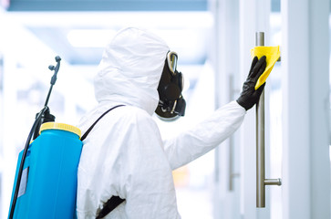 Man in protective hazmat suit washes door handles in office to preventing the spread of...
