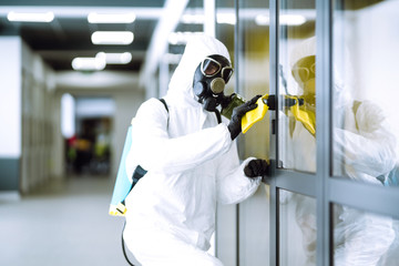 Cleaning and disinfection of office to prevent COVID-19, Man in protective hazmat suit washes office furniture to preventing the spread of coronavirus, pandemic in quarantine city.
