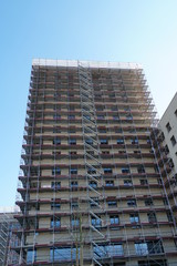 High apartment house in construction, rough building covered  by  scaffolding and protective net in frontal perspective. Switzerland in a new residential district.