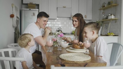 Happy family sitting around kitchen table in the morning eating breakfast together and having fun