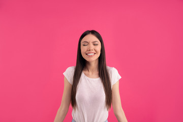 Portrait of emotiove satisfied Asian woman with natural beauty, dark combed hair, smiles happily, keeps eyes closed, wears casual t shirt, isolated on pink wall. People, ethnicity, positive emotions