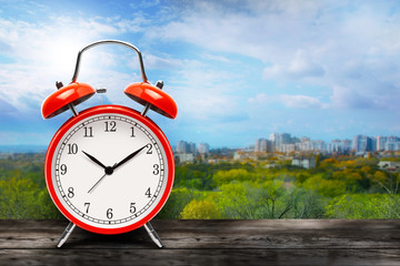 Red alarm clock on city and blue sky background