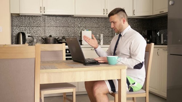 Telework. Internet conference. Businessman is wearing a shirt with a tie and shorts. He is talking on Skype with employees.