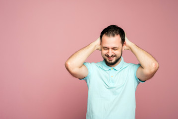 Fototapeta na wymiar A face of a bearded man on the pink background. A man is glad. A man is happy. Smiling man is pleased. A man with closed-eyes from joy. A man is holding hands behind his head
