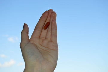 Beautiful female hand holds a medical pharmaceutical pill capsule from coronavirus covid-19 for the treatment of diseases and viruses on a blue sky background