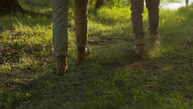 Rear view following shot of legs of male and female hikers walking on green grass through the forest