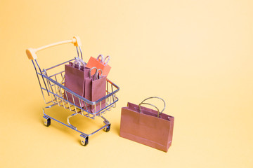 small paper bags in, miniature shopping trolley on a yellow background stands, copy space, online...