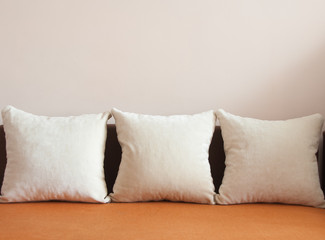 Orange fabric sofa with three white pillows. Pink background. Home concept. Copy space