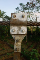 iron clamps, bolts, nuts and steel ropes on a suspension bridge in the morning against a backdrop of trees. close up 