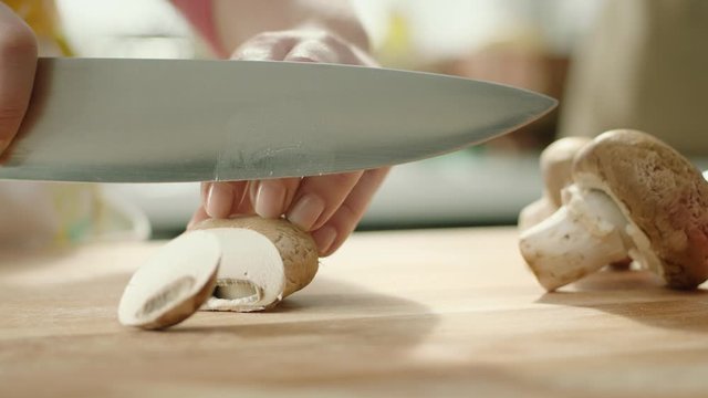 hands chopping fresh mushrooms on a cutting board with a knife, slow motion..