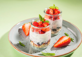 Yogurt granola parfait with strawberries and chia seeds. Healthy delicious dessert for breakfast. Mint green bright spring summer background