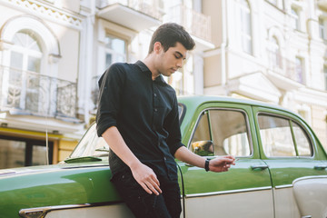 Fototapeta na wymiar Portrait of a model young handsome sexy male brunette guy with dark skin Turkish Middle Eastern brunette posing smoking a cigarette near old retro car on the street