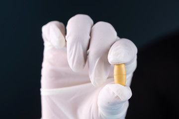 gloved hand holding a pill, cure to the coronavirus pandemic,covid-19
