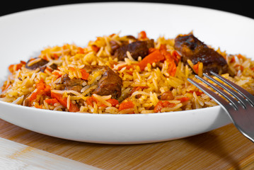 The concept of Oriental cuisine. National Uzbek pilaf with lamb meat in a white plate on a black background. Popular traditional dish of Eastern cuisine