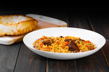 The concept of Oriental cuisine. National Uzbek pilaf with lamb meat, tandoor flatbread on a black background. A popular traditional dish of Eastern cuisine.