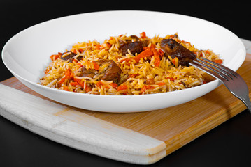 The concept of Oriental cuisine. National Uzbek pilaf with lamb meat in a white plate on a black background. Popular traditional dish of Eastern cuisine