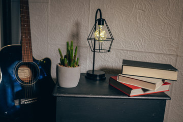 Obraz premium detail of the corner of a comfortable room with guitar, books, cloth stool, plant and a lamp